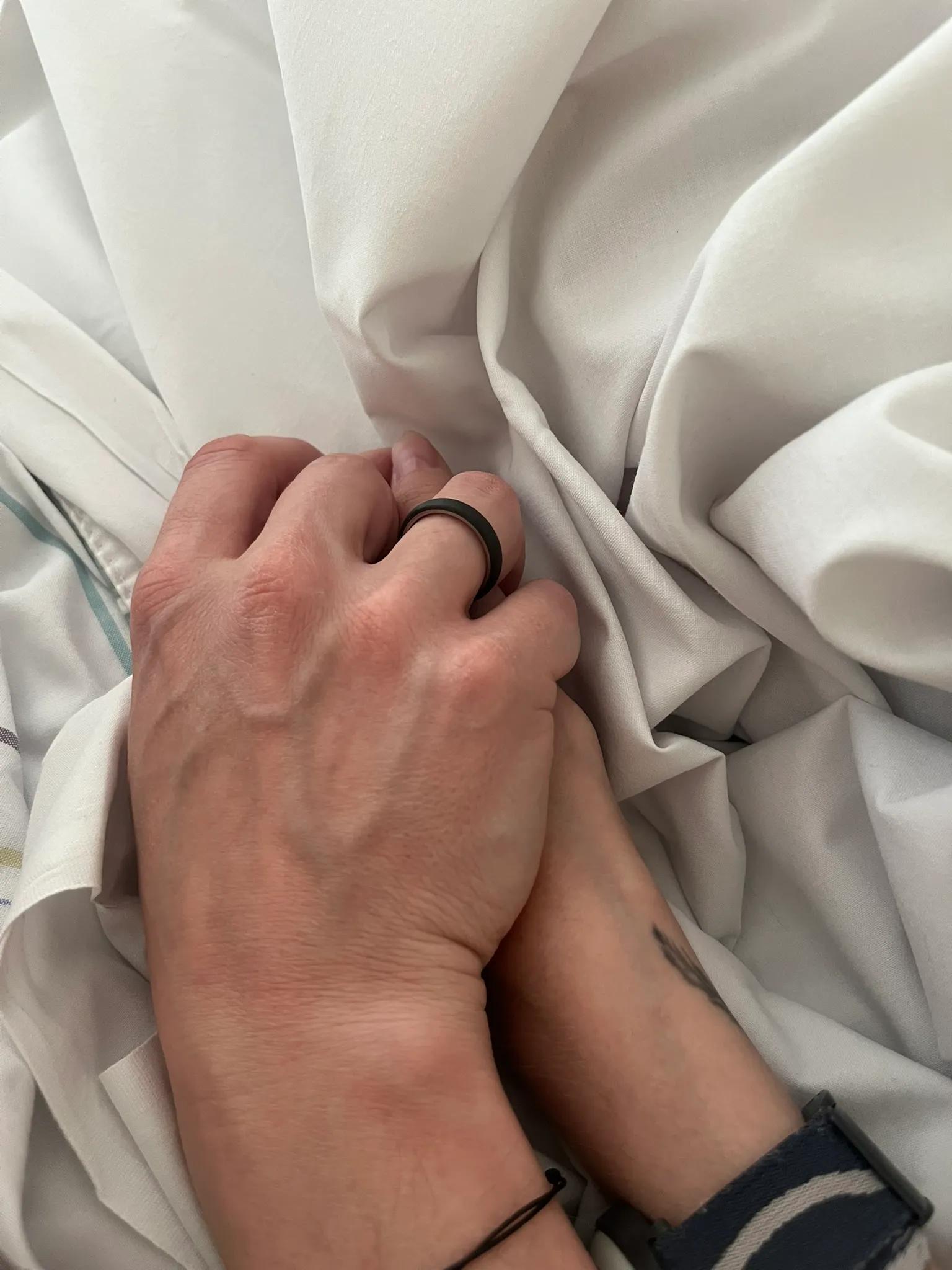 Nærbillede af Julie og Brians hænder, der holder om hinanden ovenpå et lagen i en hospitalsseng.