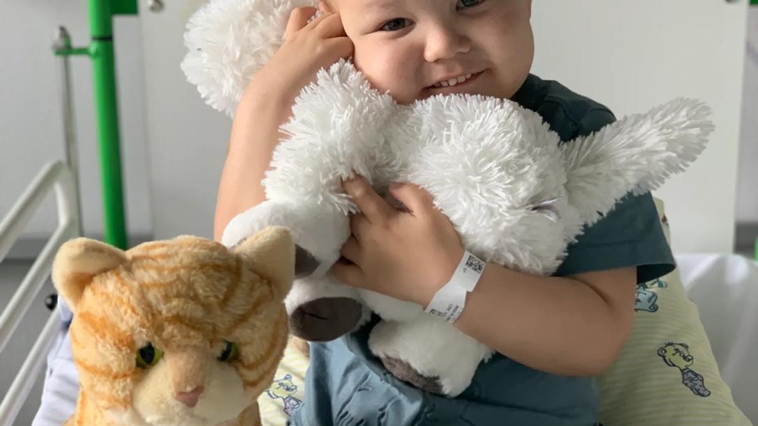 Liam sidder i hospitalssengen og krammer sin bamse 