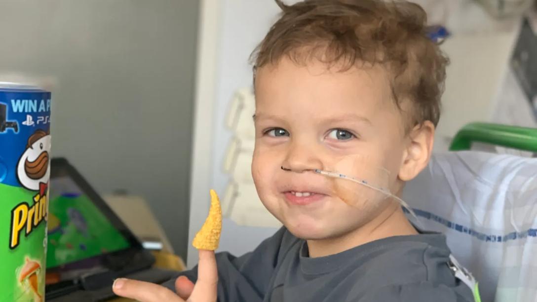 Liam sidder i hospitalssengen og spiser chips