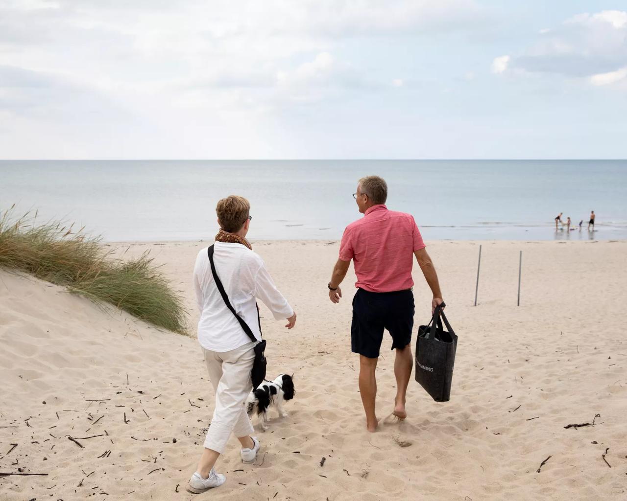 Et ældre par med en hund går i sandet ned mod havet