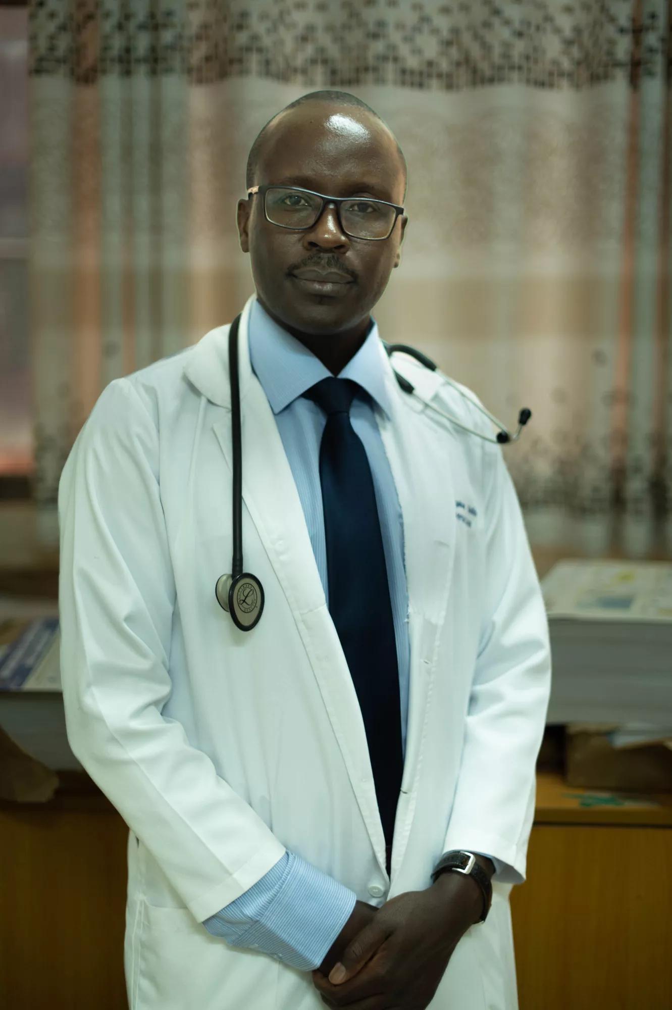 A man wearing a shirt, tie and a smock. He is a doctor. 