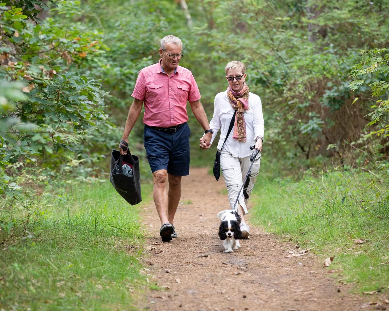 Et ældre par går tur i skoven hånd i hånd.