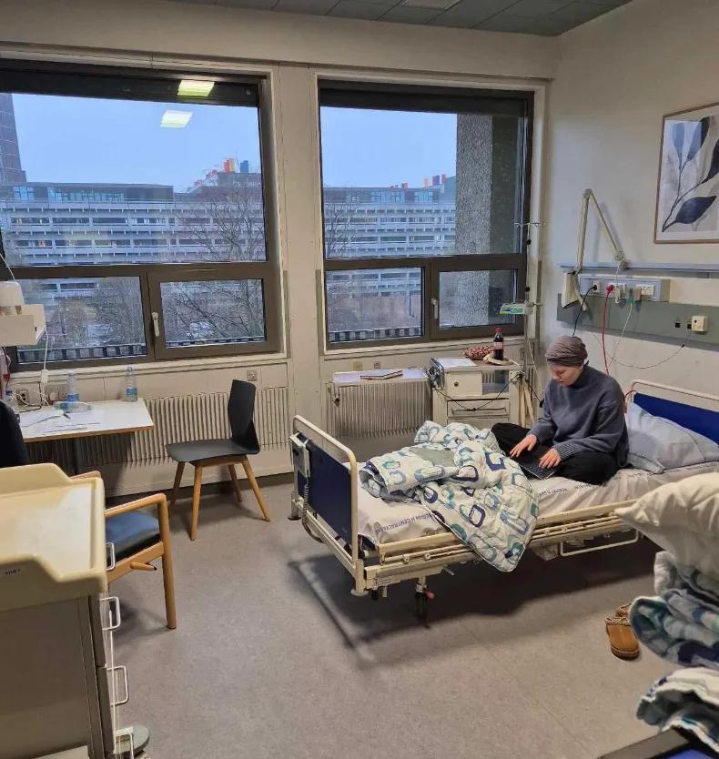 Marie sidder i sin hospitalsseng med en bærbar computer foran sig. 