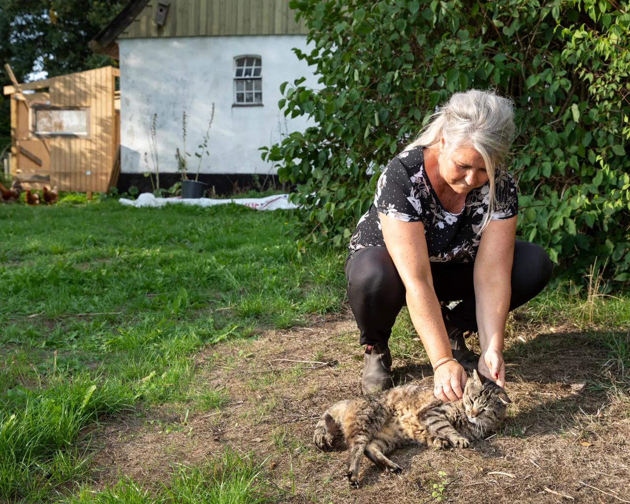 Kvinde sidder på hug og kæler med en kat i solen