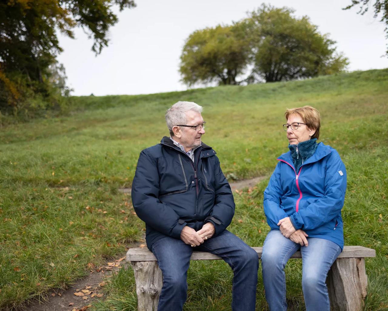 Et ældre par sidder på en bænk og taler sammen
