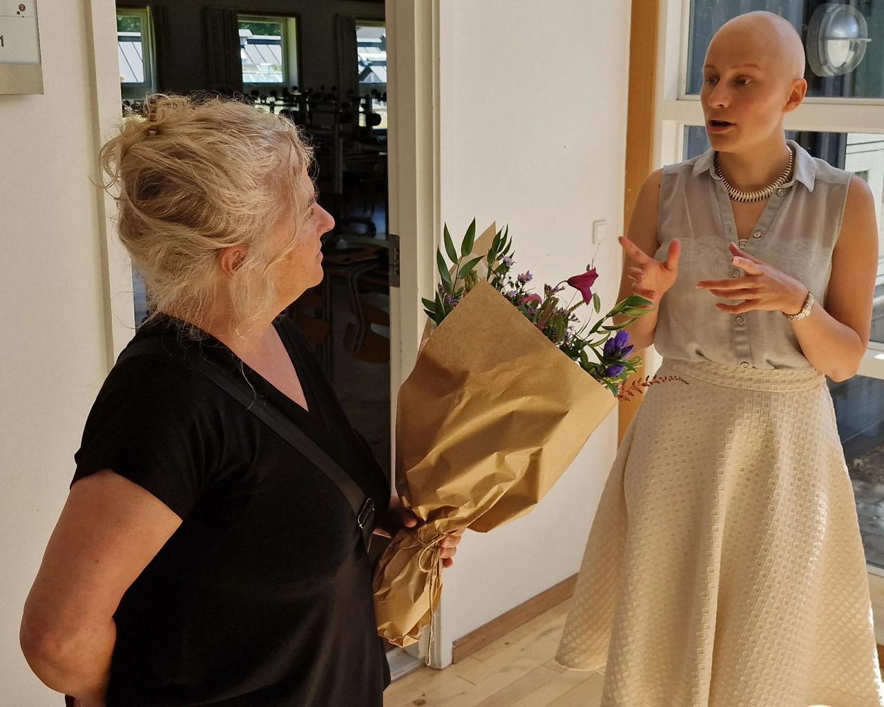 Lisa ser overrasket på kvinde, der overrækker hende blomster foran eksamenslokalet. 