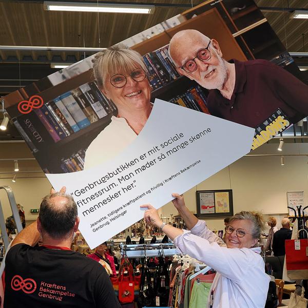 Distriktschef, Kim Steen Carlsen,  og Jeanette hænger den store planche op ved indgangspartiet til butikken. 