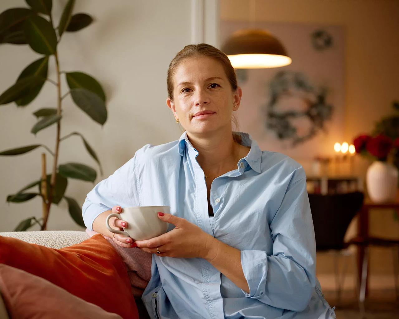 Kvinde, der sidder i stuen og drikker kaffe, nyder livet