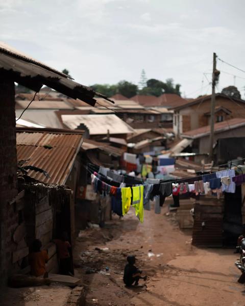 A small boy sits centrally in the image under a clothesline in Kampala, Uganda.