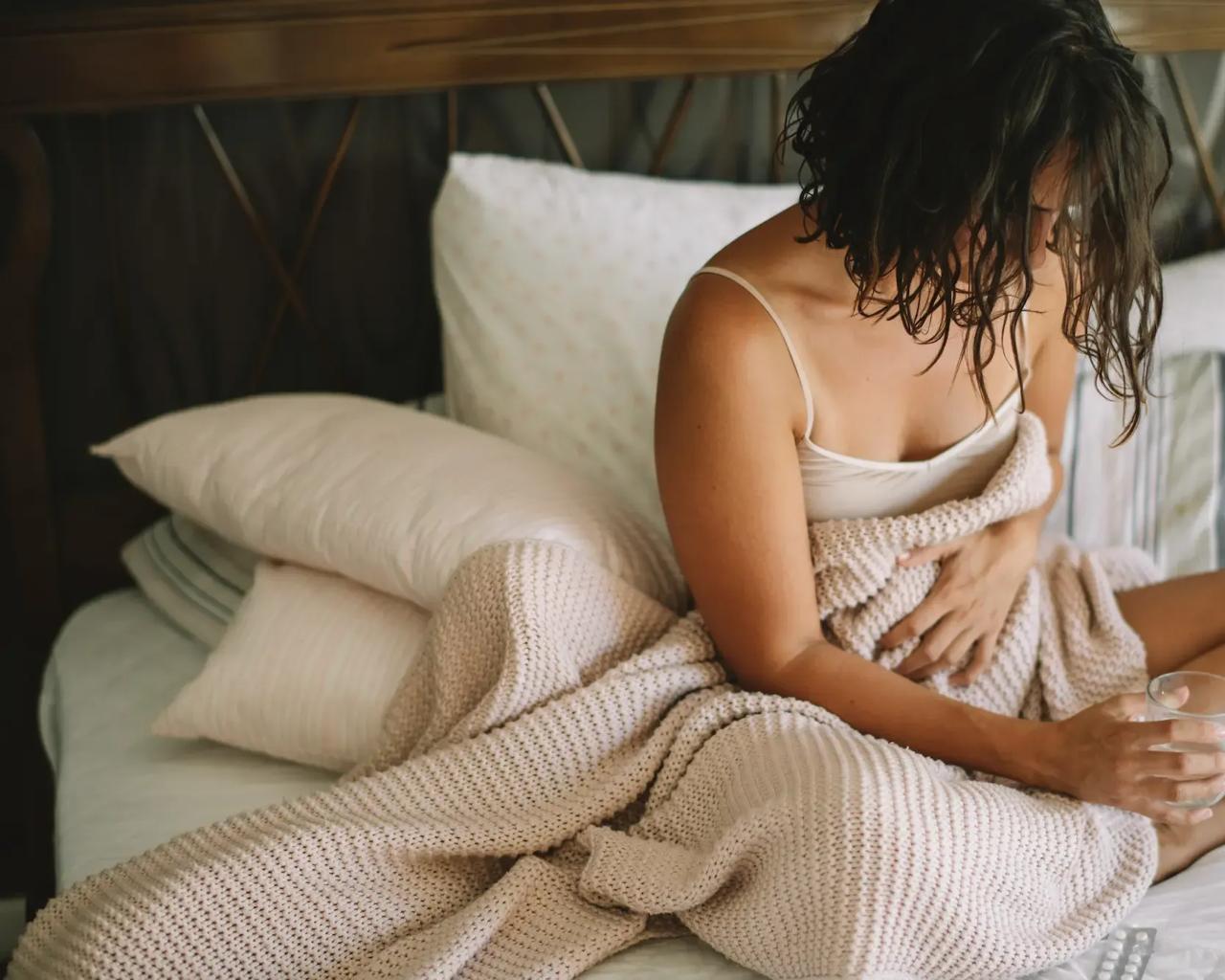 Kvinde sidder i sin seng med et glas vand og holder sig på maven
