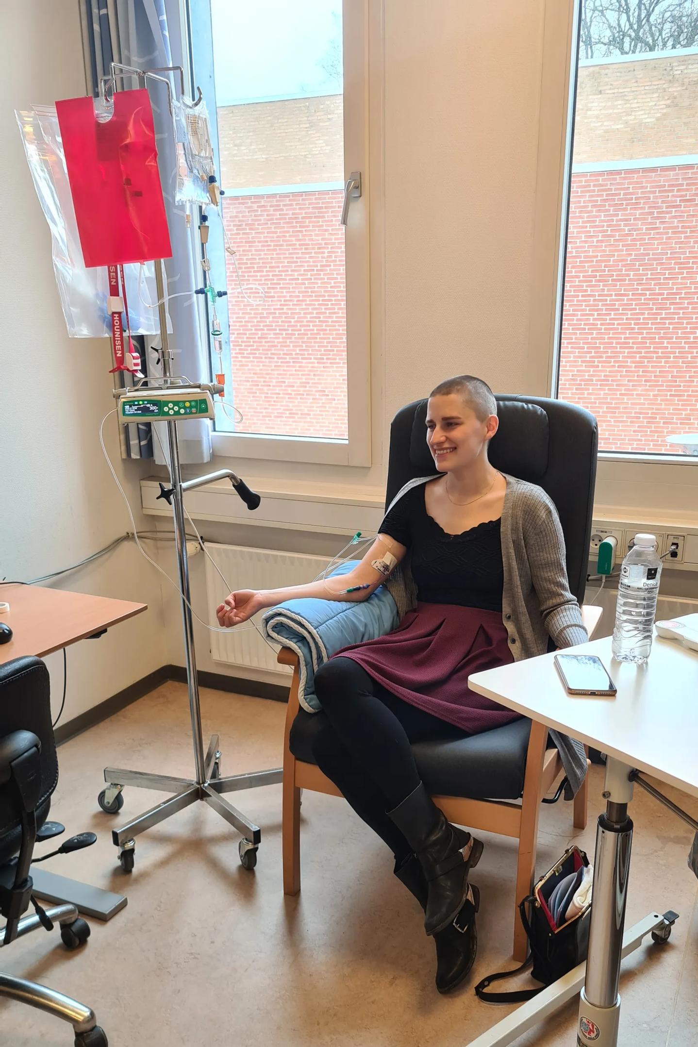 Lisa sidder i lænestol ved siden af dropstativ på kemostue. 