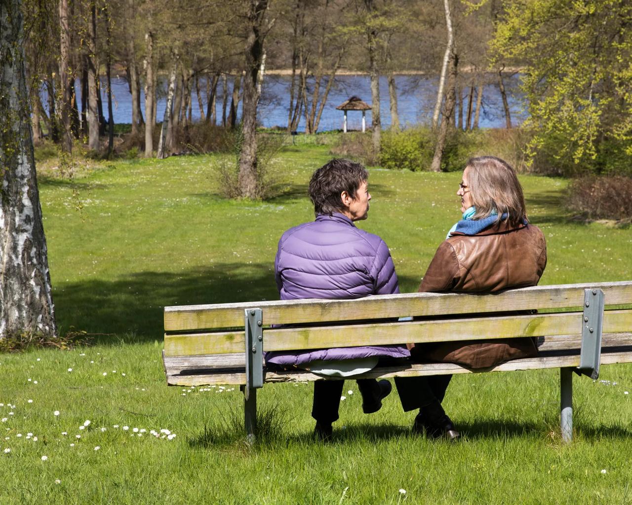 To kvinder sidder og taler sammen på en bænk i solskin