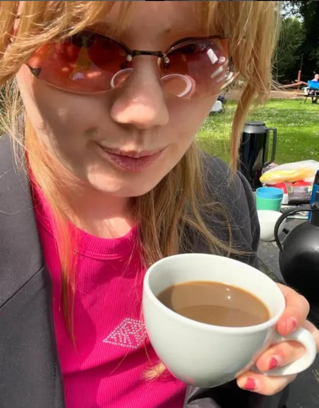 Marie står med solbriller og en kop kaffe i hånden.