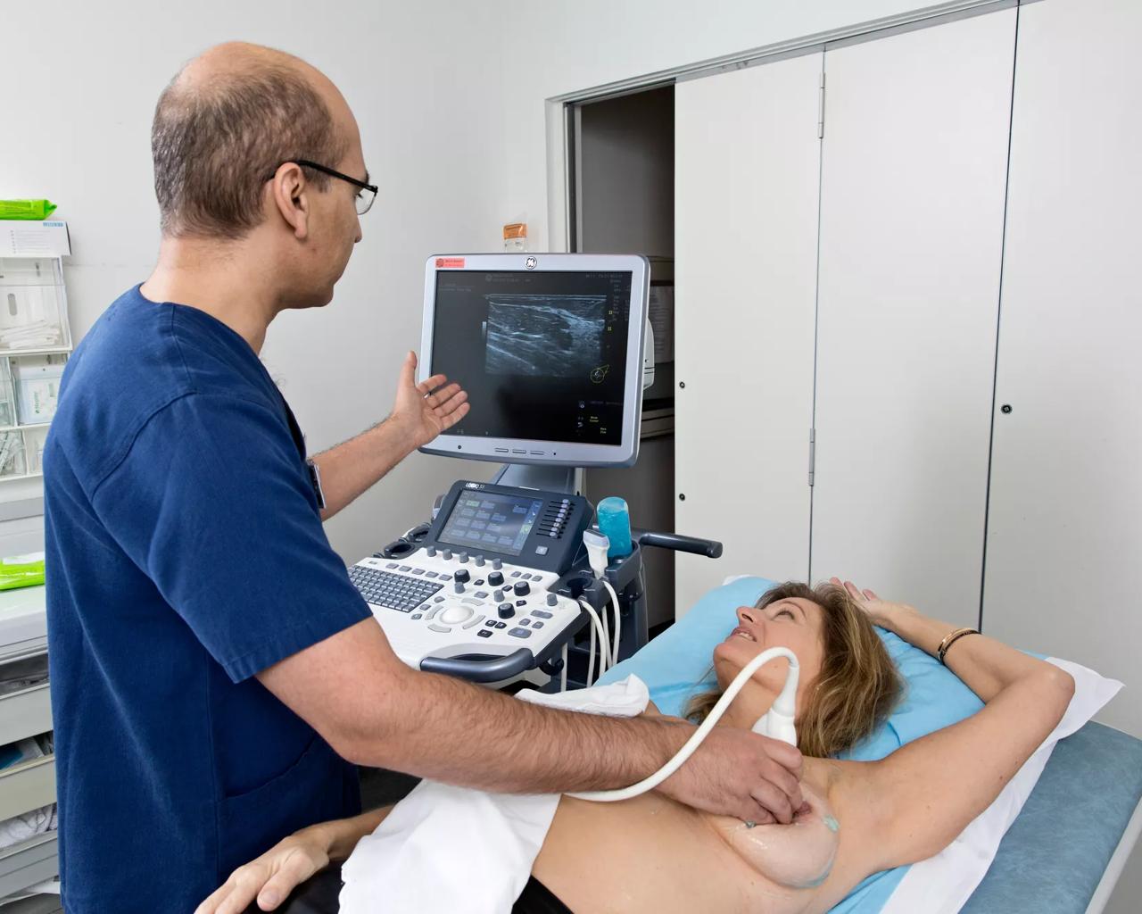 Læge scanner en kvindes bryst mens de kigger på skærmen