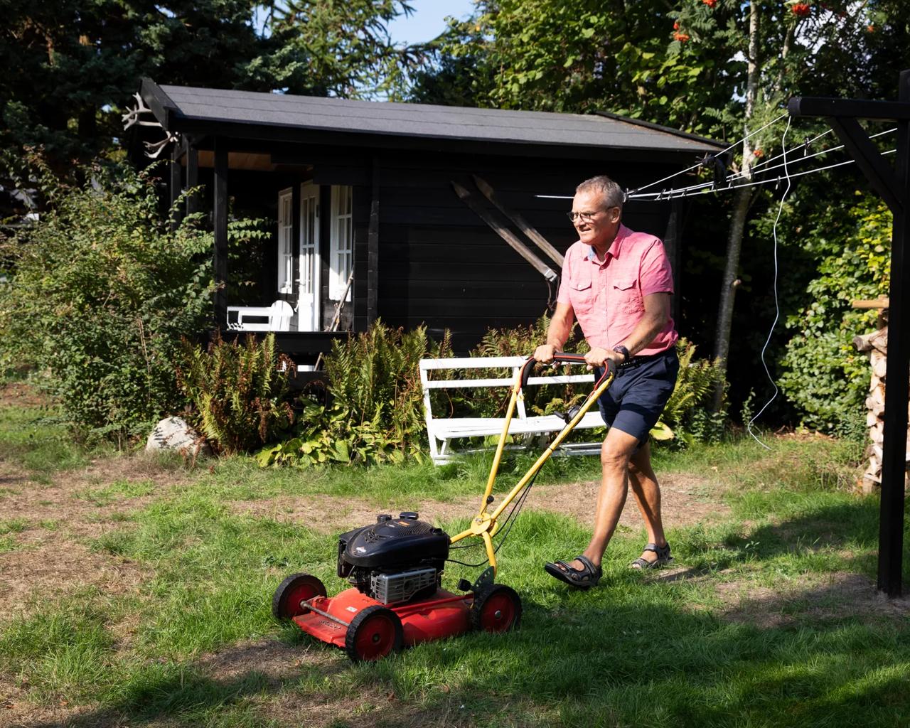 Mand i lyserød skjorte slår græs ved et sommerhus