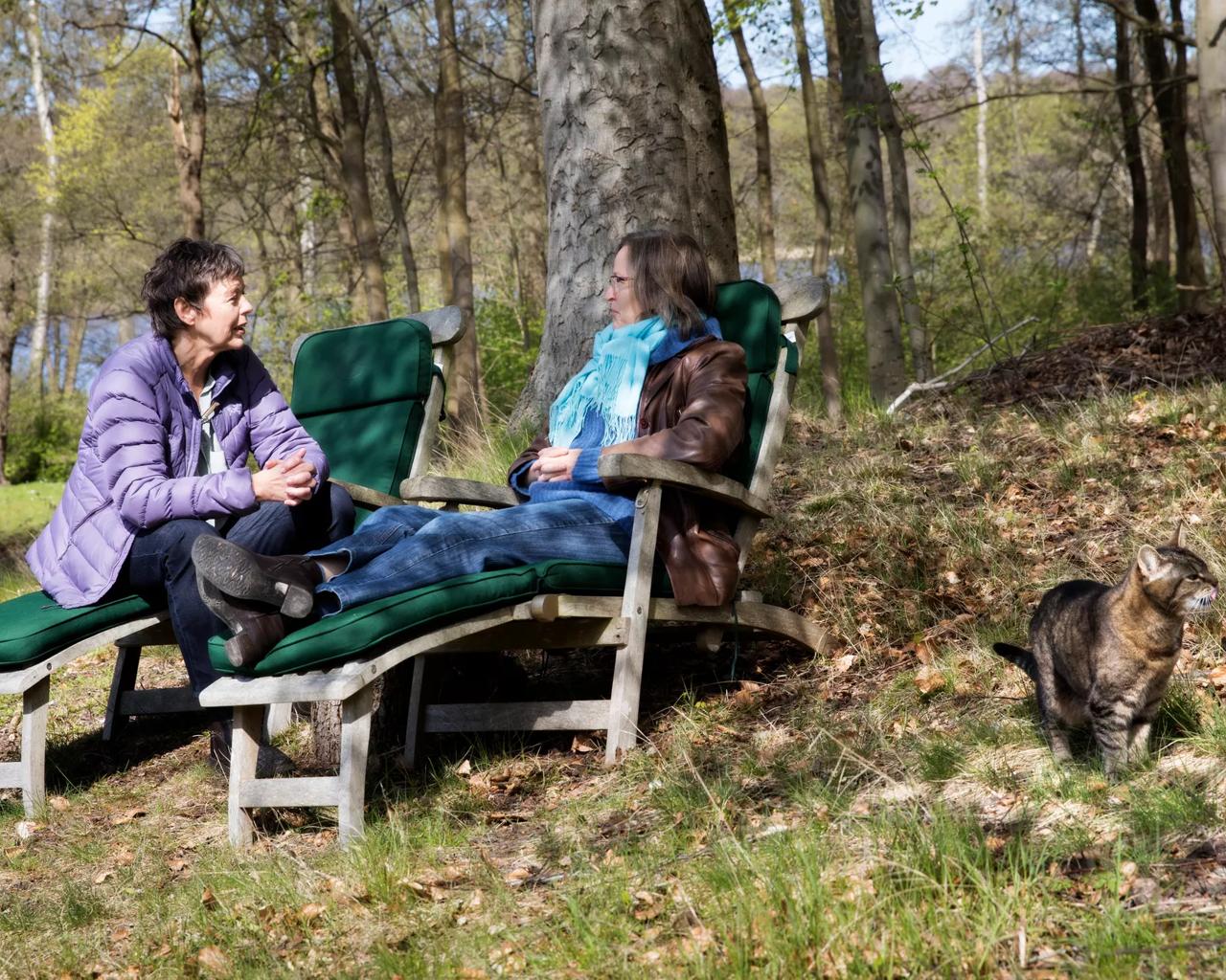 To kvinder sidder udenfor i en have om efteråret og taler 