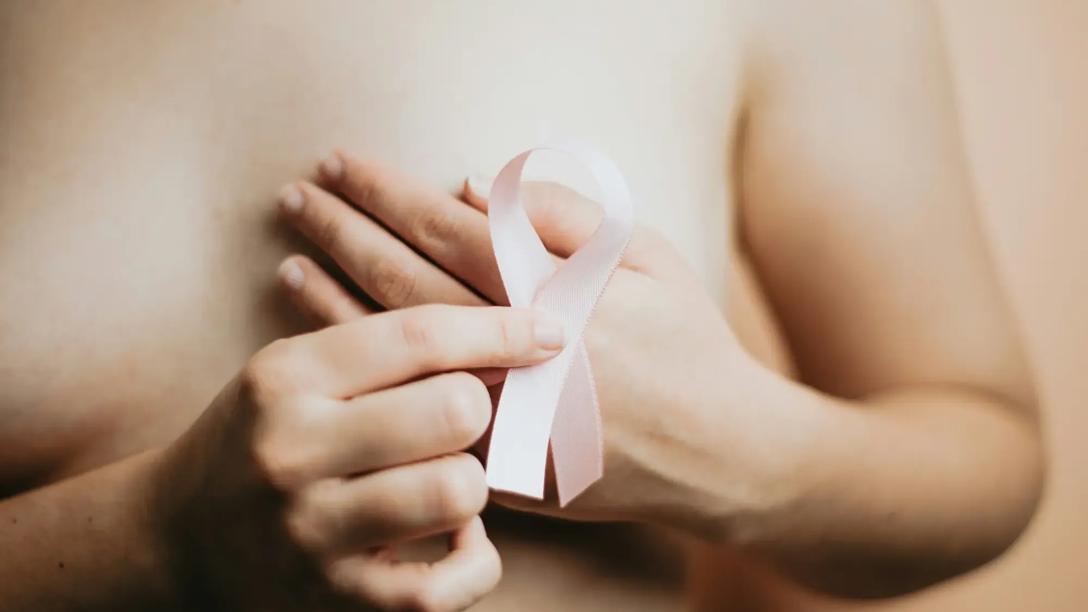 Foto af kvinde, der holder en lyserød brystkræftsløjfe foran sit nøgne bryst