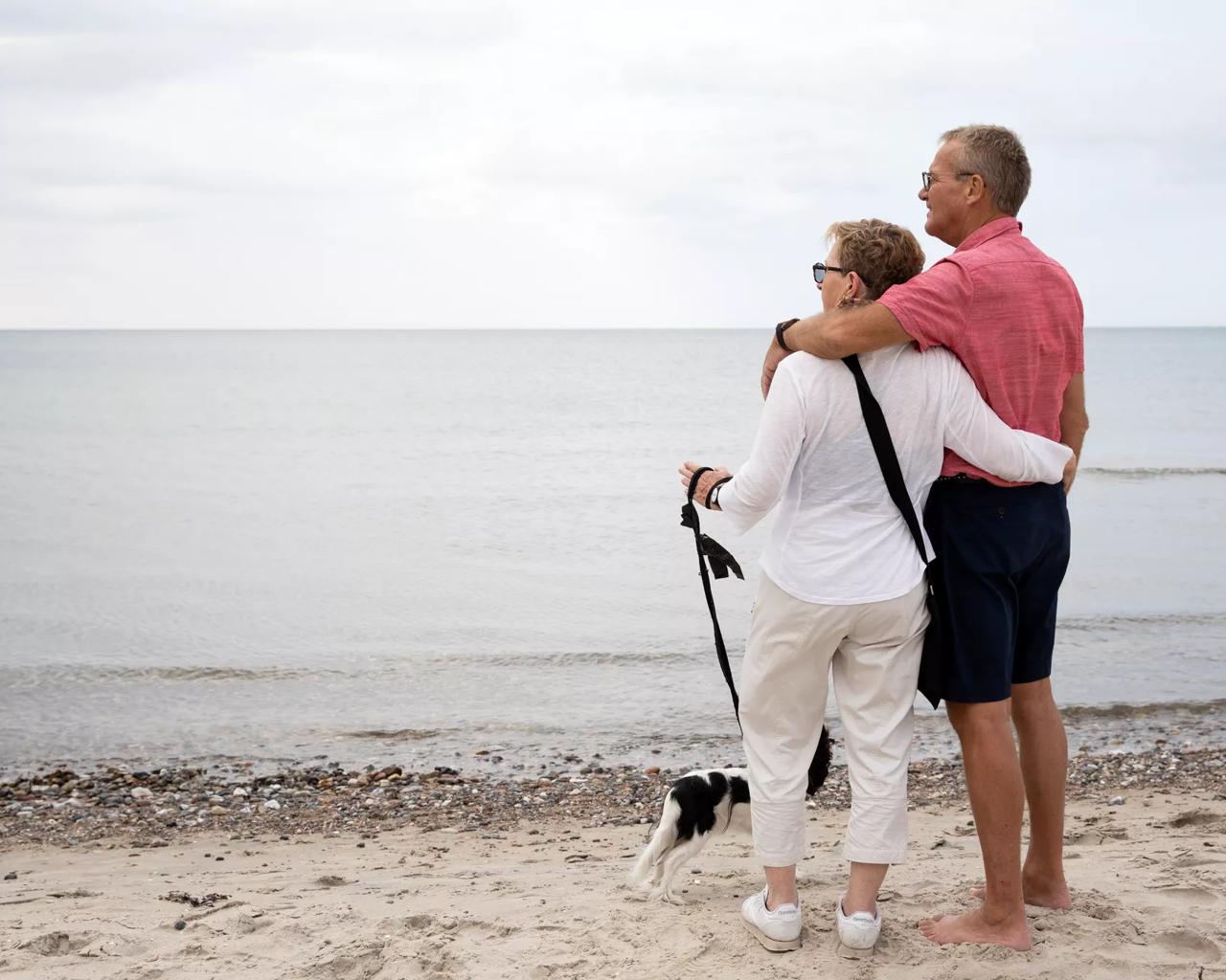 Ældre par går hånd i hånd ved stranden