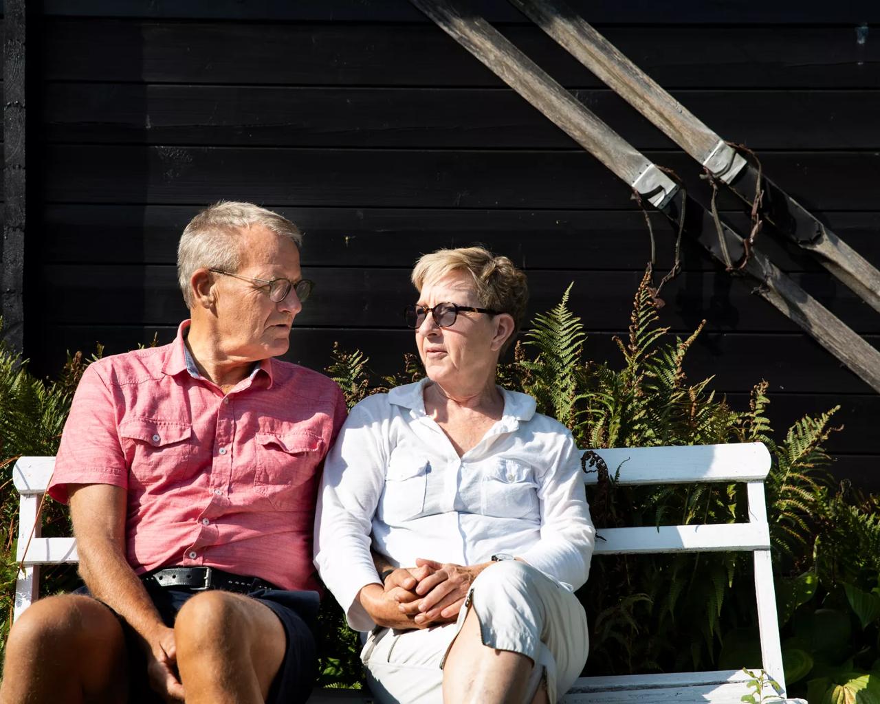 Ægtepar sidder på en bænk i solen og taler sammen