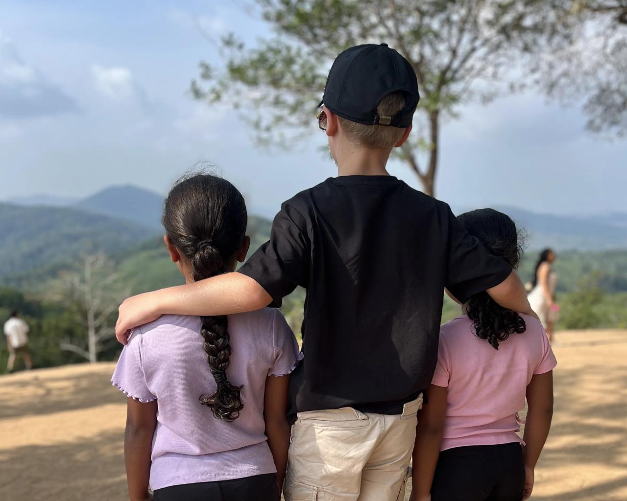 tre børn bagfra. den midterste ældste dreng har armene om sine to mindre søstre.