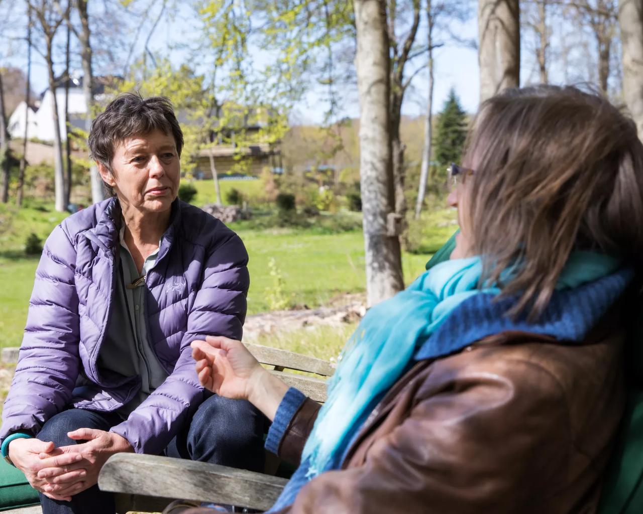 To kvinder sidder ude i en forårskov og taler sammen